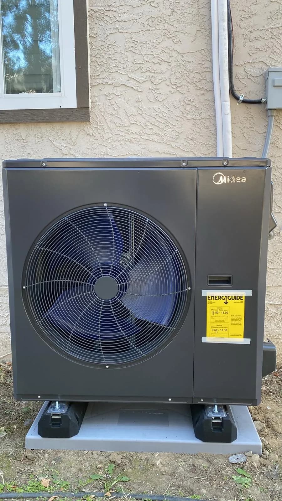 Midea central heat pump installed beside a stucco home